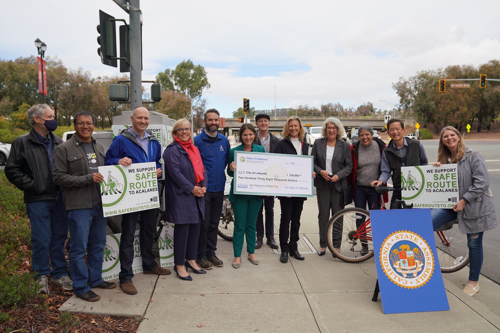 An image of a group of people, including Assemblymember Bauer-Kahan. They are holding signs to show their support for the project. The Assemblymember is holding an oversized check made out to the City of Lafayette.